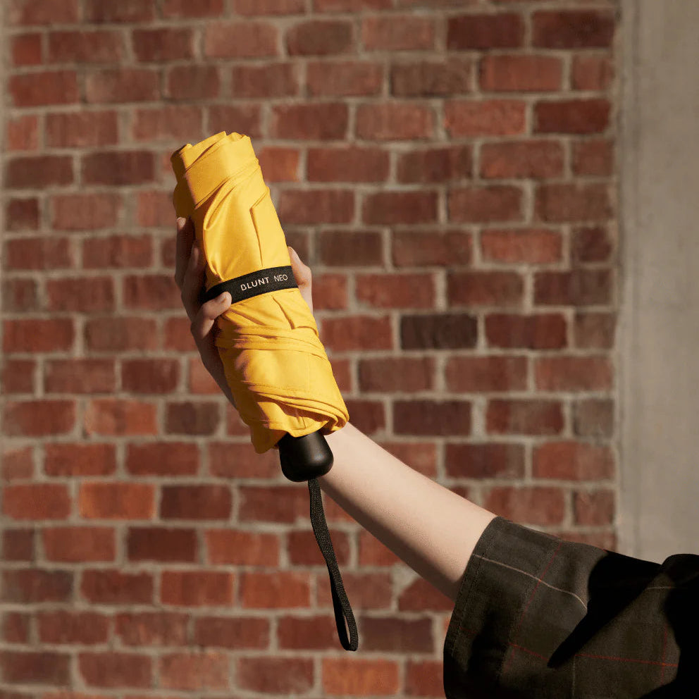 Yellow umbrella held by a person against a brick wall