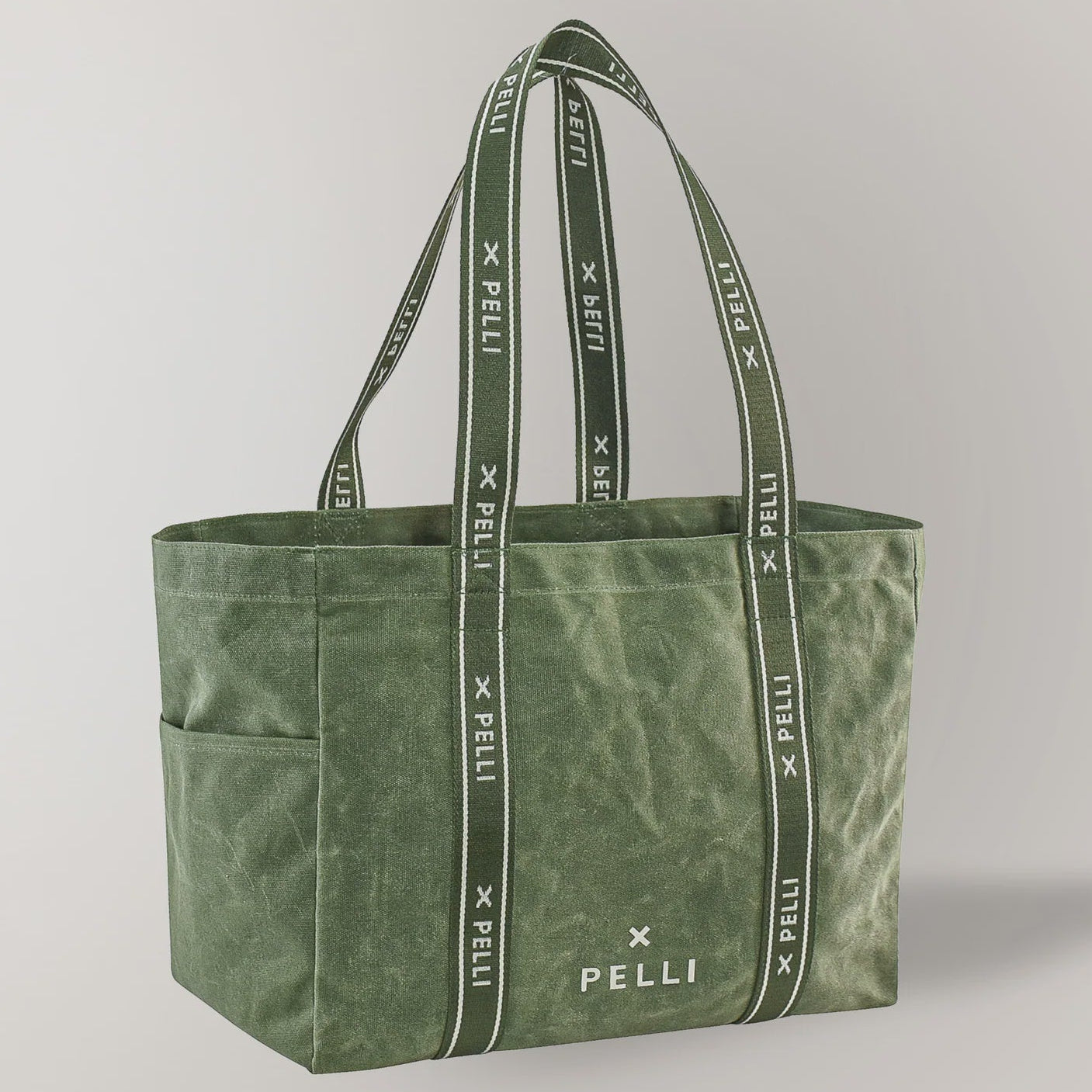 An olive green canvas tote bag with matching shoulder straps featuring a repeating white 'PELLI X PELLi' logo pattern, shown on a light gray background.