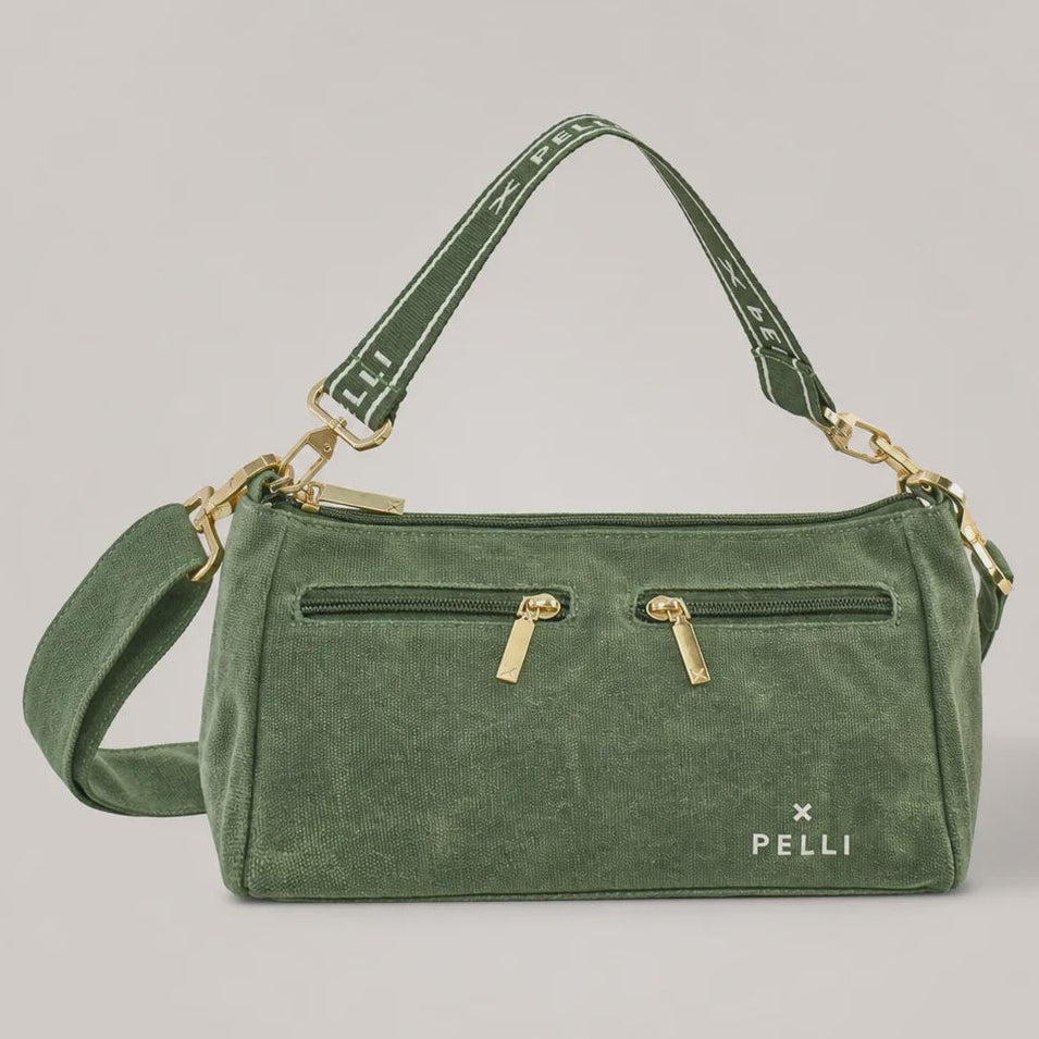 An olive green velvet shoulder bag with gold-tone hardware, featuring a front zippered pocket with two gold zipper pulls, a matching green shoulder strap, and a detachable crossbody strap, set against a solid light gray background.